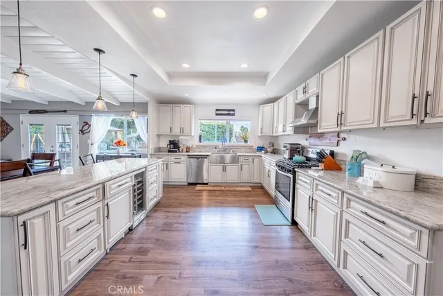 a kitchen with stainless steel appliances granite countertop white cabinets a sink a stove a refrigerator and microwave with wooden floor