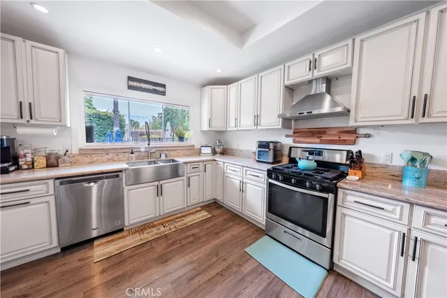 a kitchen with stainless steel appliances granite countertop a stove a sink dishwasher and a dining table with wooden floor