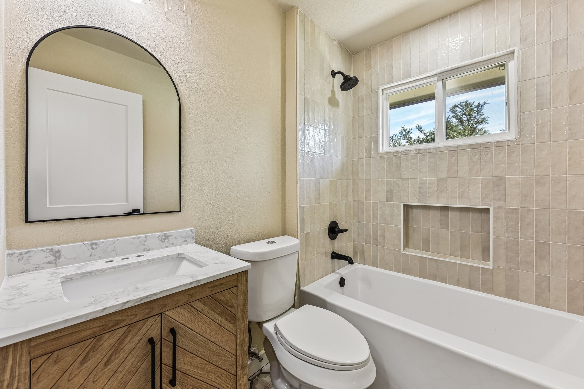 7523 Glenhill Road Austin, TX 78752 - Photo 21 of 38 A well-appointed bathroom with a sleek vanity and a tiled bath area, featuring a window for natural light.