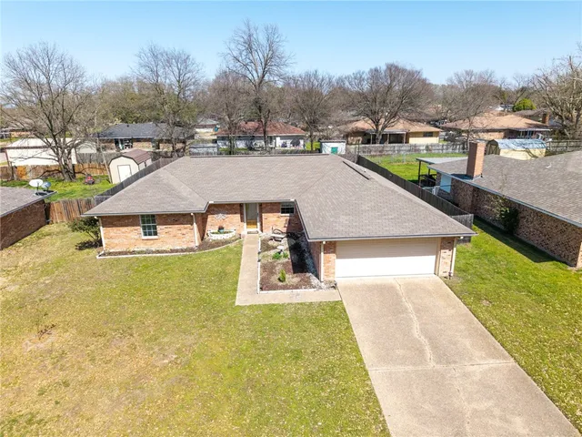 a view of a white house with a yard plants and large tree