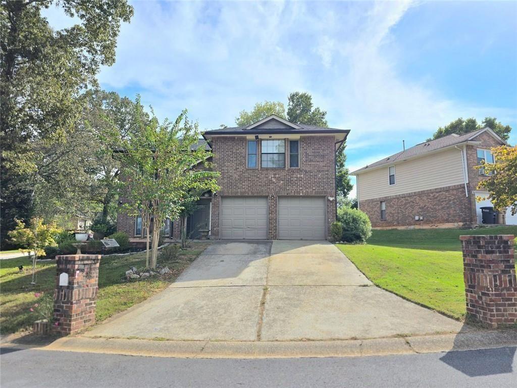 a view of a brick house with a small yard and large trees