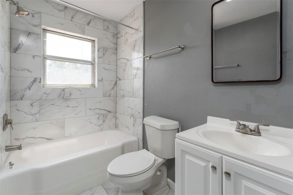 1101 Kennedale Sublett Road Kennedale, TX 76060 - Photo 23 of 35 White tile surround bathtub with shower fixture, single vanity with white cabinet storage, wall-mounted mirror, and white toilet