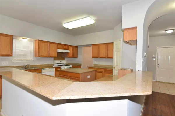 a large kitchen with kitchen island a large counter top space a sink wooden floor and a large window