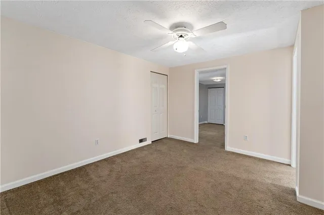 an empty room with chandelier fan and windows