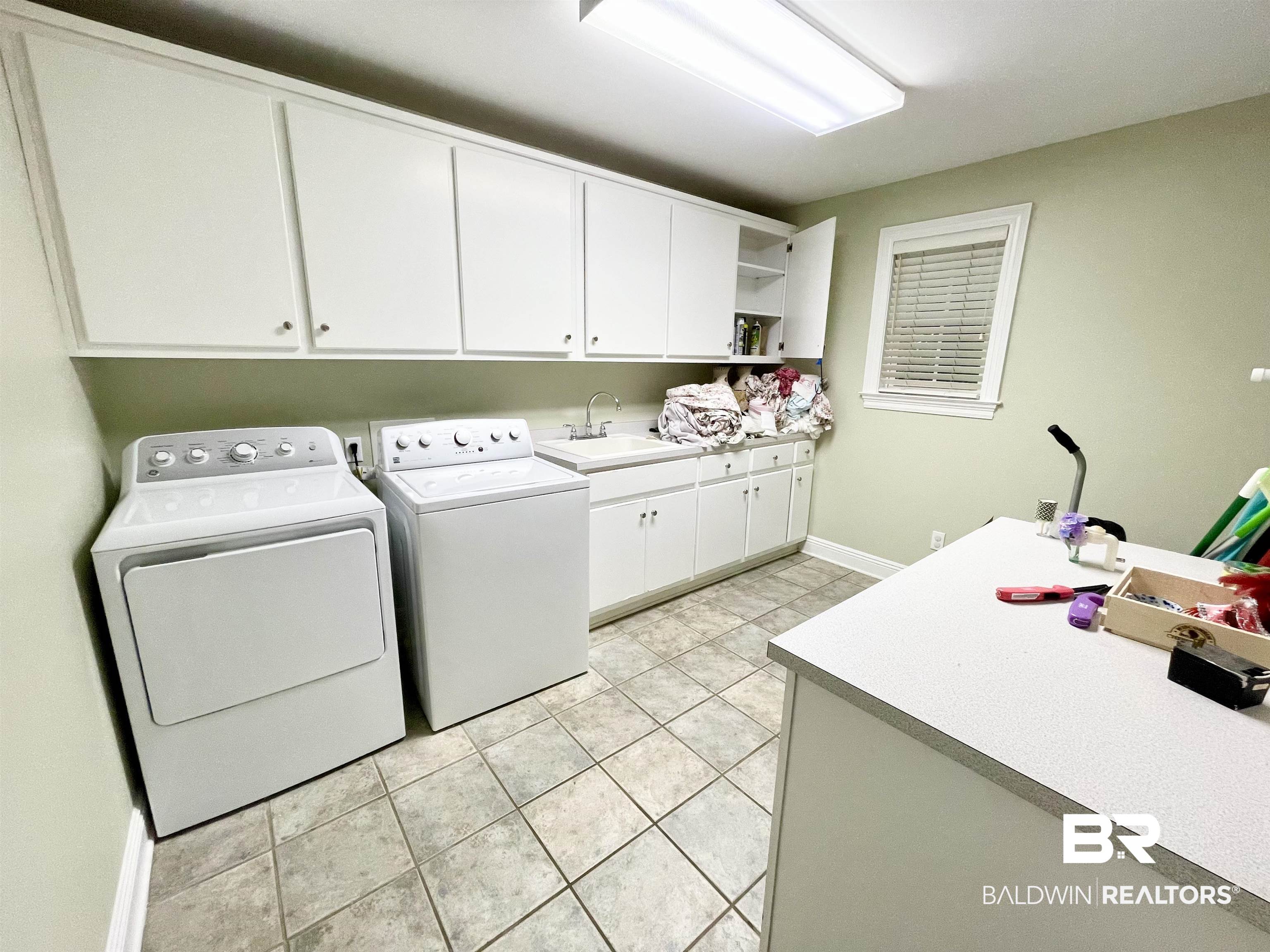 202 Potters Mills Road Daphne, AL 36526 - Photo 23 of 29 Large laundry room featuring cabinets, light tile patterned floors, washer and dryer, folding table, and sink