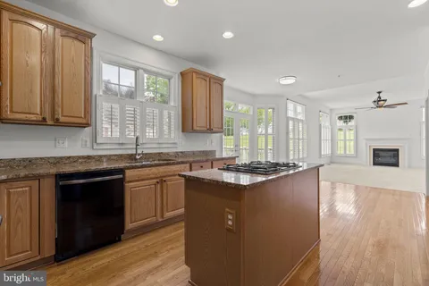 a kitchen with stainless steel appliances granite countertop a stove a sink a refrigerator white cabinets and wooden floor