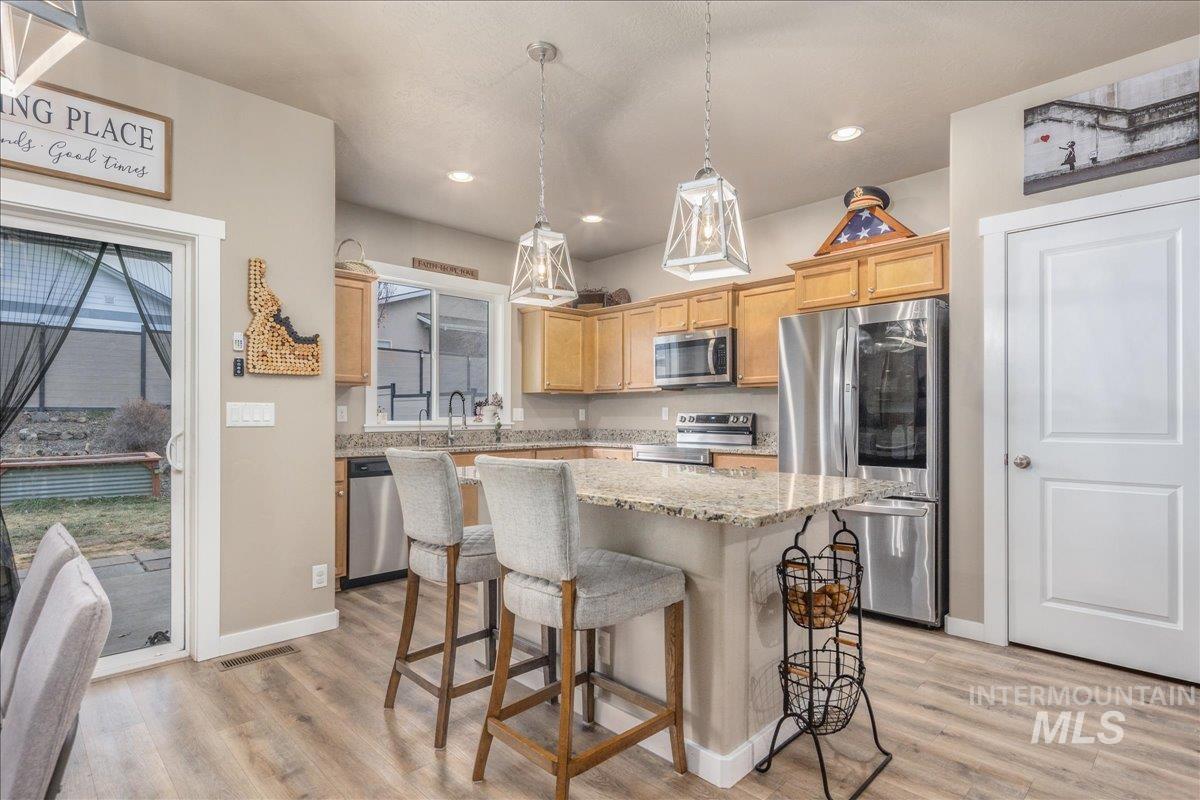 5668 West Old Ranch Street Boise, ID 83714 - Photo 18 of 44 Kitchen featuring appliances with stainless steel finishes, a breakfast bar, light stone countertops, pendant lighting, and a kitchen island