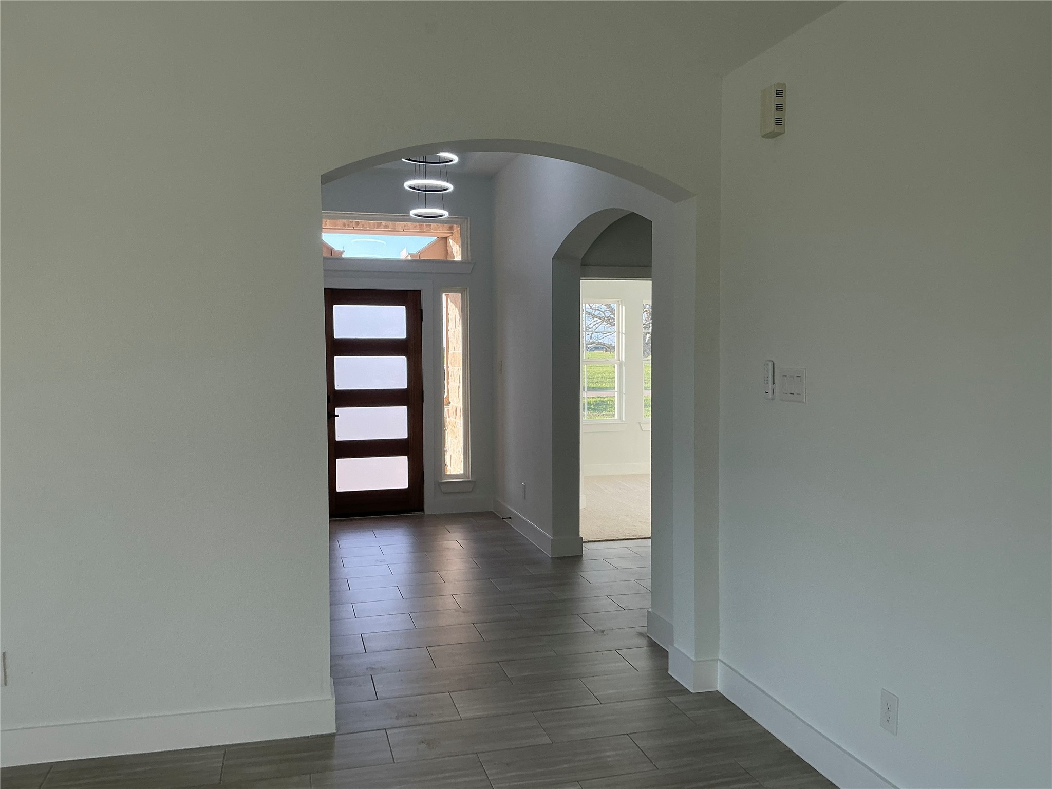471 Buffalo Trail Angleton, TX 77515 - Photo 2 of 35 Bright entryway featuring modern tile flooring and a stylish wooden front door with frosted glass panels. Arched openings lead to a well-lit space with large windows showcasing outdoor views.