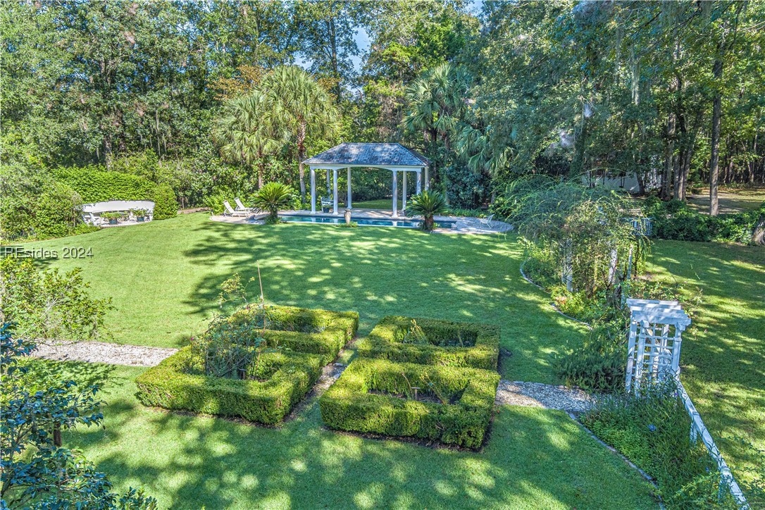 92 Dean Hall Road Seabrook, SC 29940 - Photo 11 of 99 In the North elevation yard / quadrant, the primary residence's flowering beds / parterre garden / grounds / crescent bench and pool, shaded comfort canopy and pergola