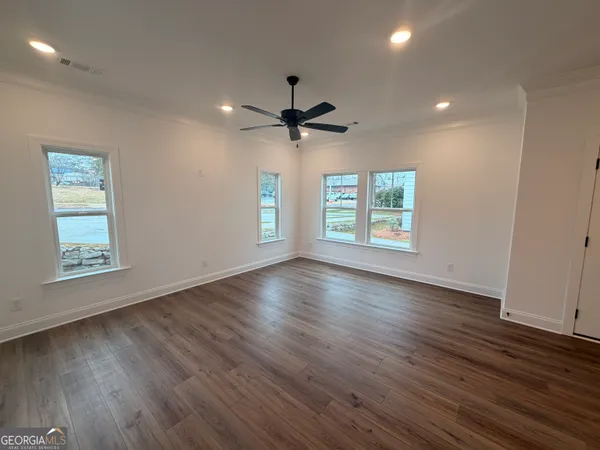 an empty room with wooden floor chandelier fan and windows