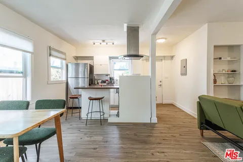 a kitchen with stainless steel appliances granite countertop a refrigerator a stove top oven a dining table and chairs with wooden floor