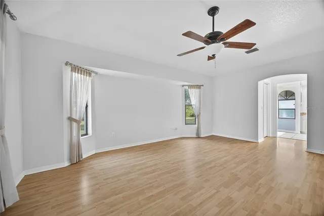 an empty room with wooden floor a ceiling fan and windows