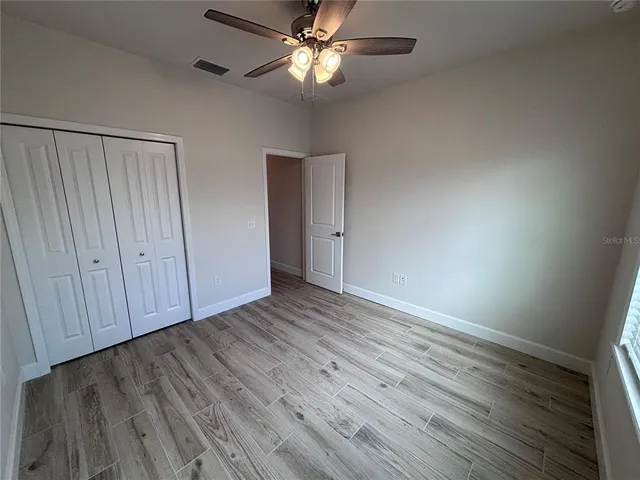 an empty room with wooden floor fan and windows