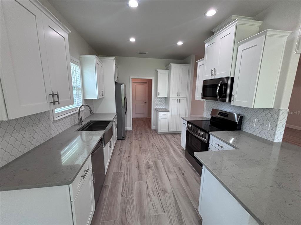 6686 Southwest 11th Lane Gainesville, FL 32607 - Photo 9 of 24 a kitchen with stainless steel appliances a stove top oven a sink a refrigerator white cabinets and wooden floor