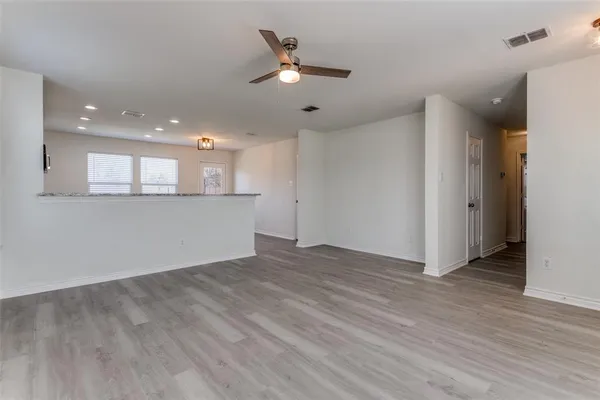 a view of an empty room with wooden floor and a ceiling fan