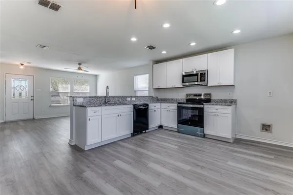 a kitchen with stainless steel appliances granite countertop a stove top oven a sink and white cabinets with wooden floor
