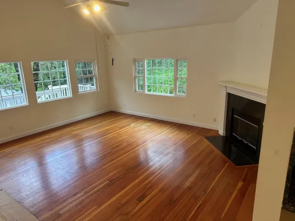 an empty room with wooden floor fireplace and windows