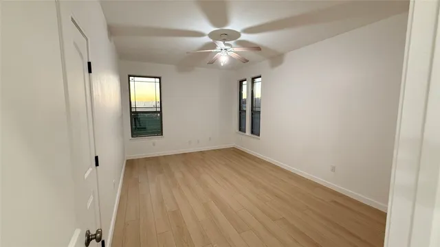 an empty room with wooden floor chandelier fan and windows