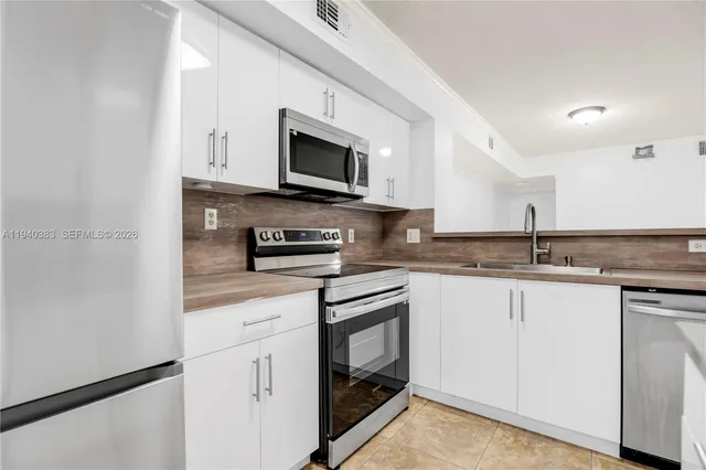 a kitchen with stainless steel appliances granite countertop white cabinets a sink a stove a microwave and a refrigerator