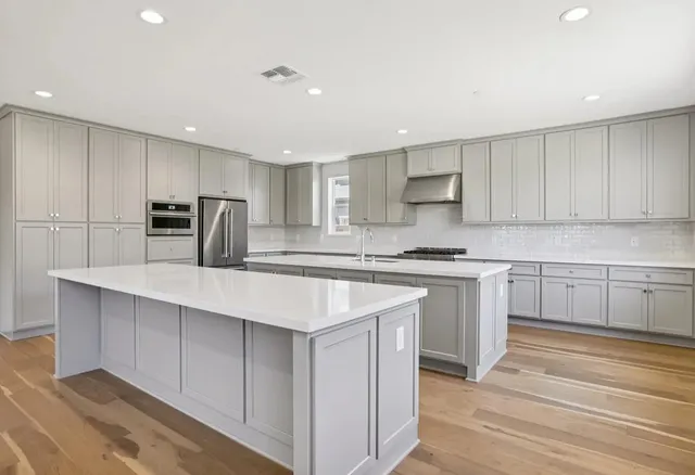 a kitchen with kitchen island a sink a stove a refrigerator and white cabinets with wooden floor