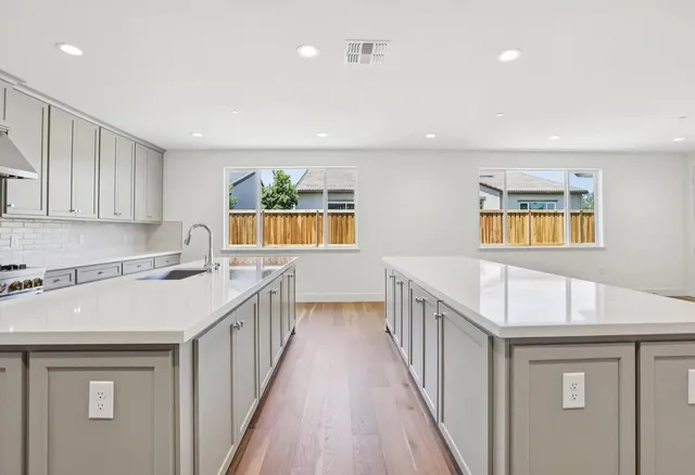 a view of an empty room with wooden floor and a kitchen