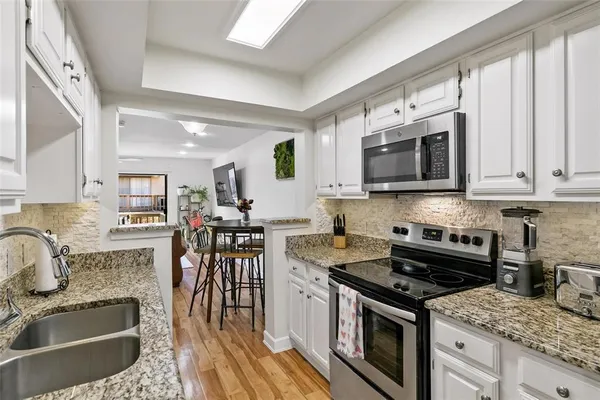 a kitchen with stainless steel appliances granite countertop a stove top oven a sink dishwasher a dining table and chairs with wooden floor