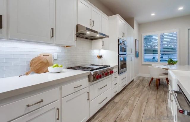 a kitchen with stainless steel appliances a white stove top oven a sink dishwasher and white cabinets with wooden floor