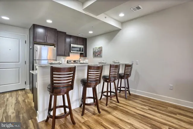 a kitchen with stainless steel appliances kitchen island granite countertop a dining table chairs and refrigerator