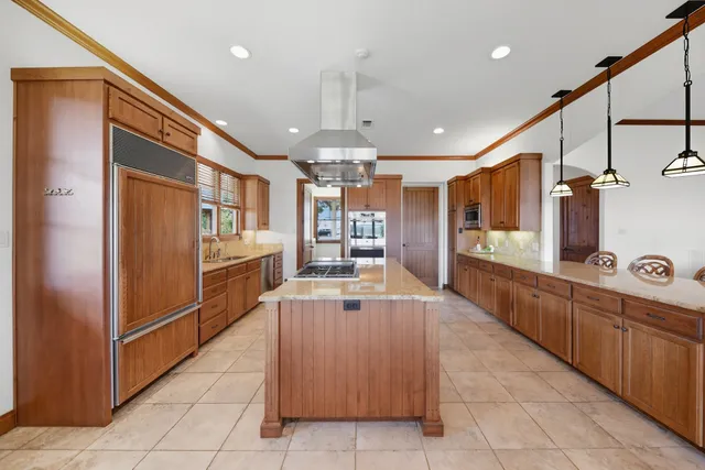a large kitchen with kitchen island a large counter top stainless steel appliances and cabinets