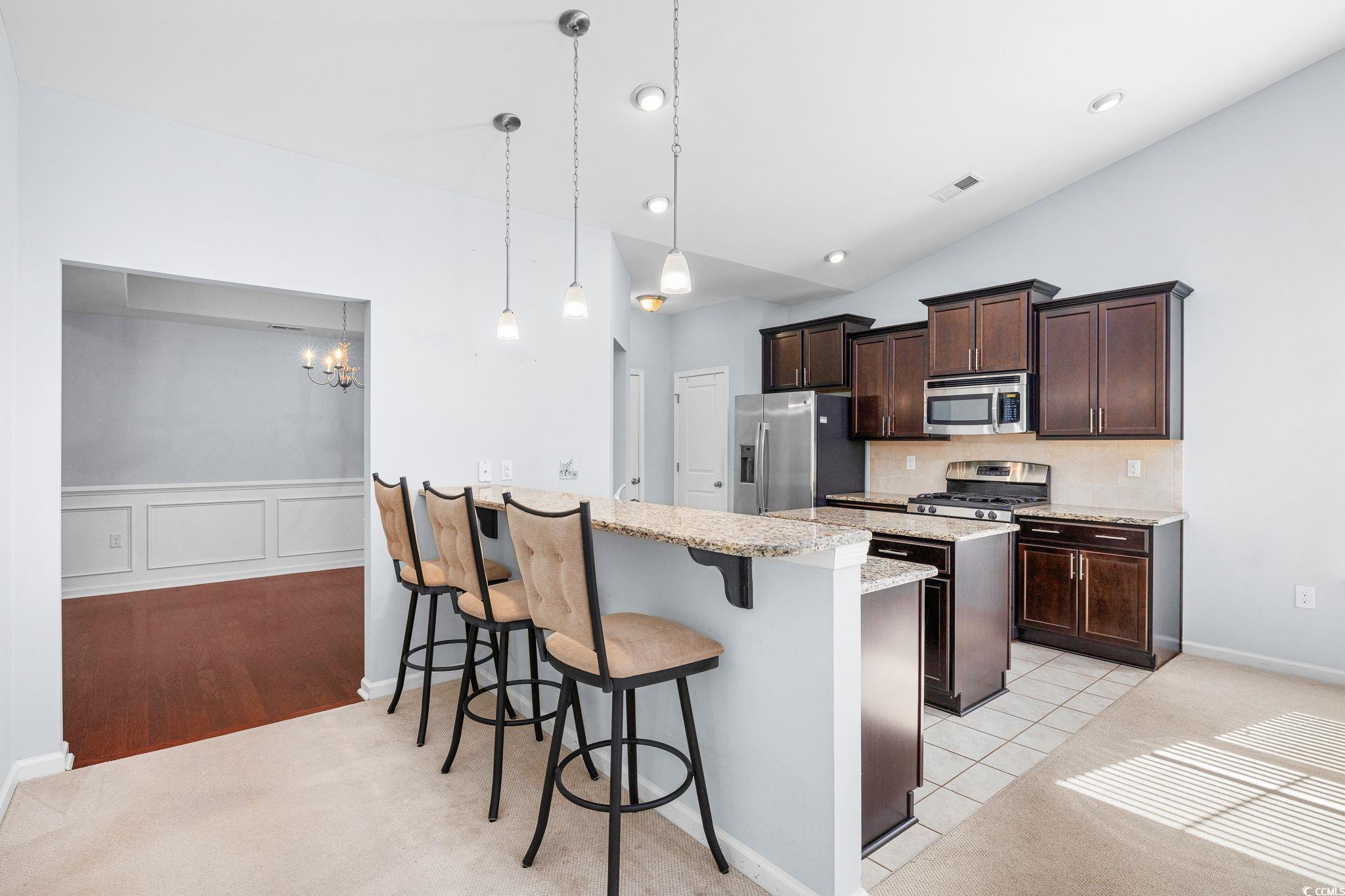 817 Arezzo Way, Unit 1001 Myrtle Beach, SC 29579 - Photo 11 of 40 Kitchen with a breakfast bar, dark brown cabinets, light stone countertops, appliances with stainless steel finishes, and a peninsula
