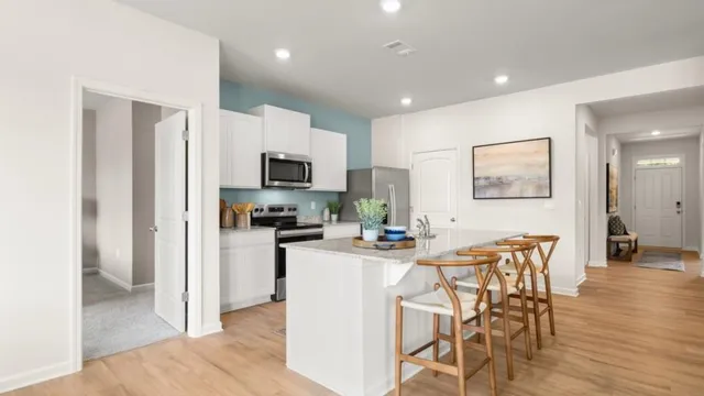 a kitchen with stainless steel appliances granite countertop a refrigerator a stove top oven a sink a dining table and chairs with wooden floor