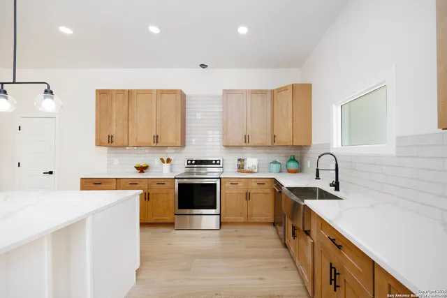 a kitchen with stainless steel appliances granite countertop a stove top oven a sink a refrigerator and white cabinets with wooden floor