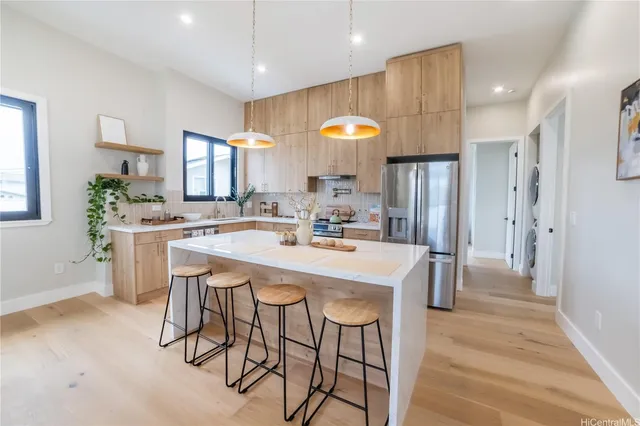 a kitchen with stainless steel appliances kitchen island granite countertop a dining table chairs and a refrigerator