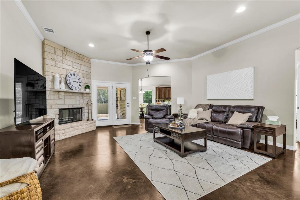 814 Springdale Circle Lorena, TX 76655 - Photo 14 of 37 Living area featuring a stone-clad fireplace with a hearth and mantel, dark concrete flooring, and crown molding
