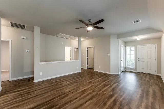 a view of an empty room with wooden floor and a ceiling fan