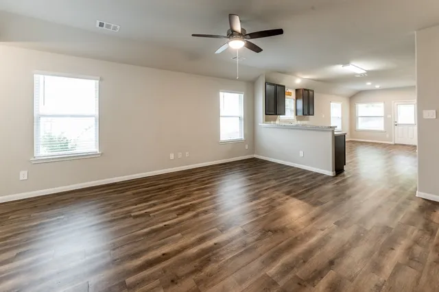 a view of a kitchen and empty room with wooden floor and a window