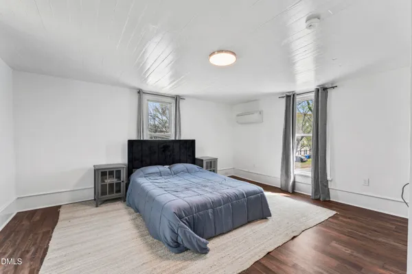 a bedroom with a bed and dresser with wooden floor