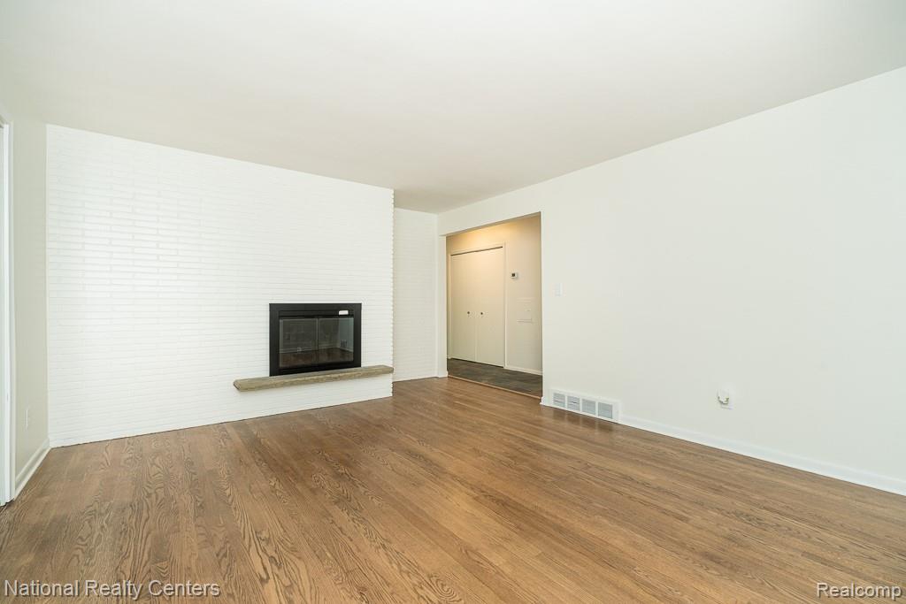 144 West Maryknoll Road Rochester, MI 48309 - Photo 21 of 38 Spacious living area featuring warm wood-finish flooring, a fireplace with brick surround and mantel, white painted walls, and a neutral color palette