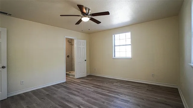an empty room with wooden floor ceiling fan and windows