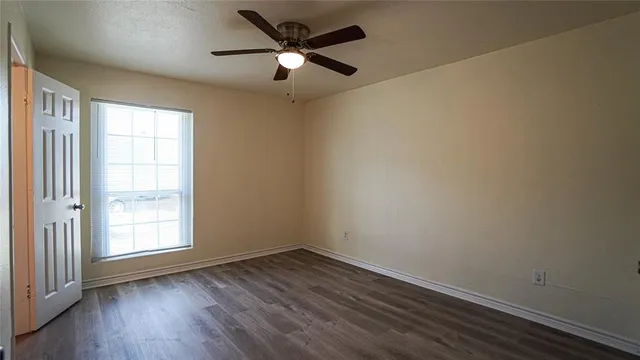 an empty room with wooden floor ceiling fan and windows