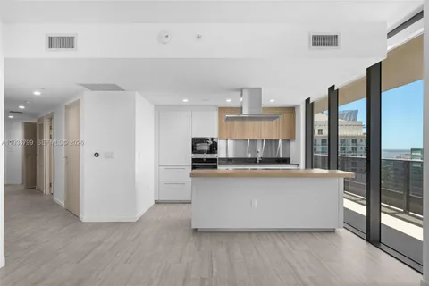 a living room with stainless steel appliances a refrigerator a sink dishwasher a stove and a large window with wooden floor