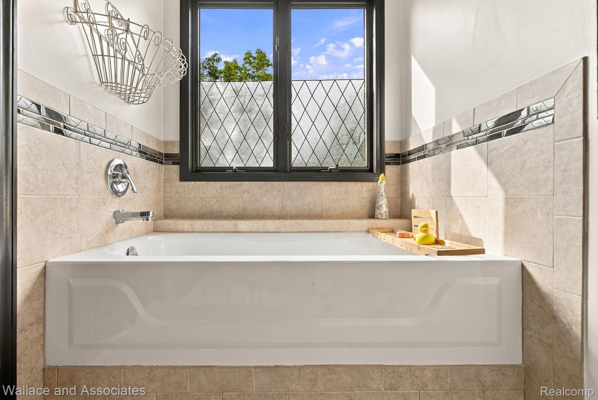 17076 27 Mile Road Ray, MI 48096 - Photo 27 of 63 Built-in bathtub with chrome fixtures, surrounded by tiled walls featuring a decorative glass mosaic accent, set below a black-framed window with patterned privacy glass