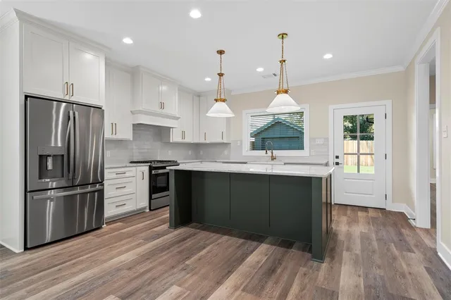 a kitchen with stainless steel appliances granite countertop a refrigerator a sink dishwasher a stove and white cabinets with wooden floor