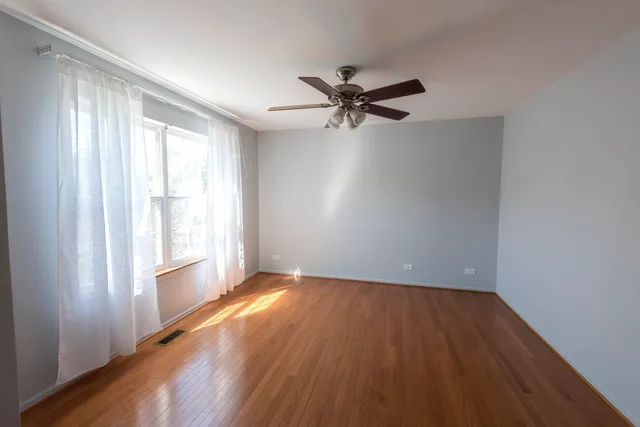 a view of empty room with wooden floor and fan