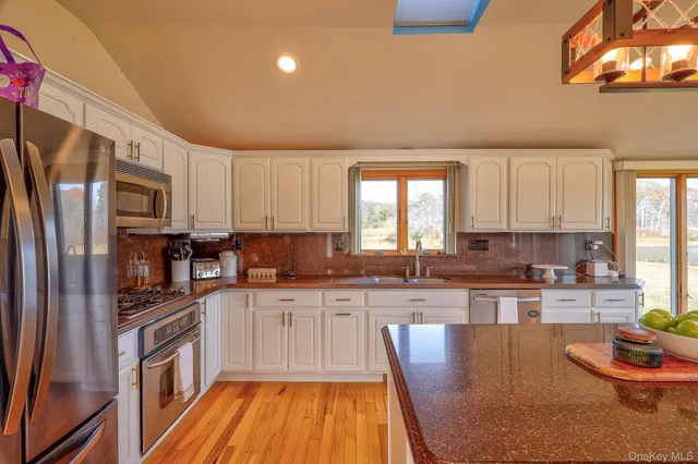 a kitchen with stainless steel appliances granite countertop a stove a sink dishwasher a refrigerator and white cabinets with wooden floor