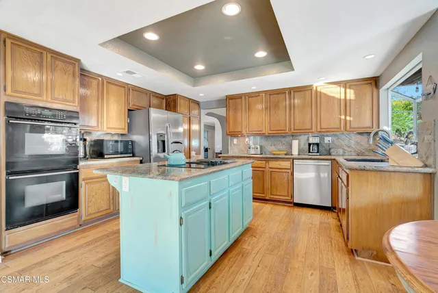 a kitchen with kitchen island granite countertop a refrigerator a sink dishwasher a stove and white cabinets with wooden floor