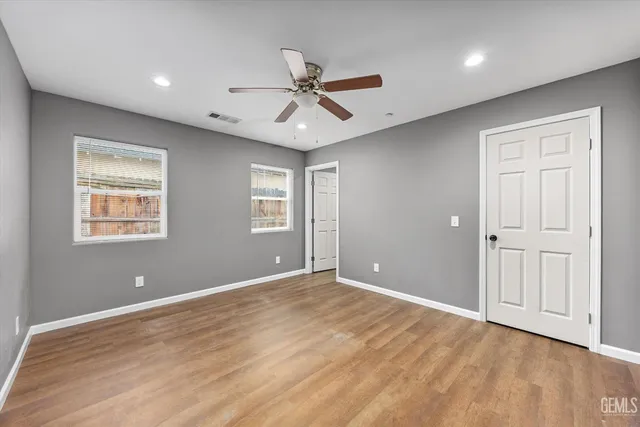 a view of an empty room with wooden floor and a ceiling fan