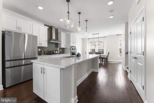 a kitchen with stainless steel appliances a refrigerator a sink dishwasher a oven a stove and white cabinets with wooden floor