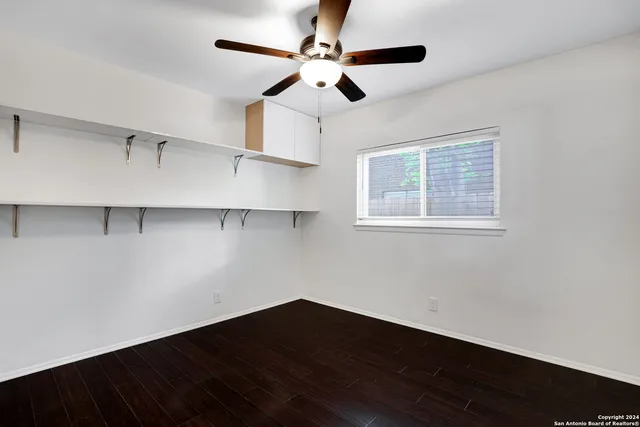 a view of an empty room with wooden floor and a ceiling fan