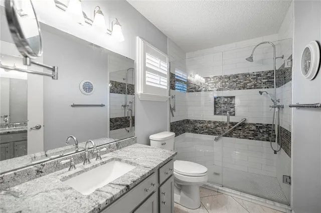 a bathroom with a granite countertop sink a toilet a mirror and shower
